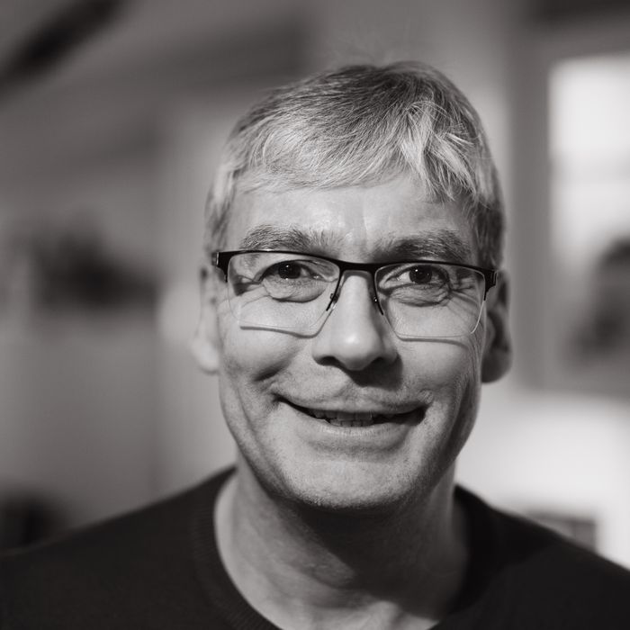 Close-up black and white portrait of a smiling man wearing glasses indoors.